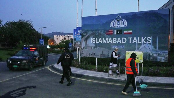 A worker cleans the street as police officers walks towards their vehicle outside a media center close to Serena Hotel, the venue for the U.S. Iran officials meeting, in Islamabad, Pakistan, Sunday, April 12, 2026. - Sputnik Afrique