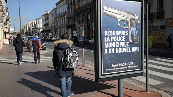 This photo taken on February 11, 2015 in downtown Beziers, southwestern France, shows a resident walking past a municipality campaign poster showing an automatic 7.65 handgun - Sputnik Afrique