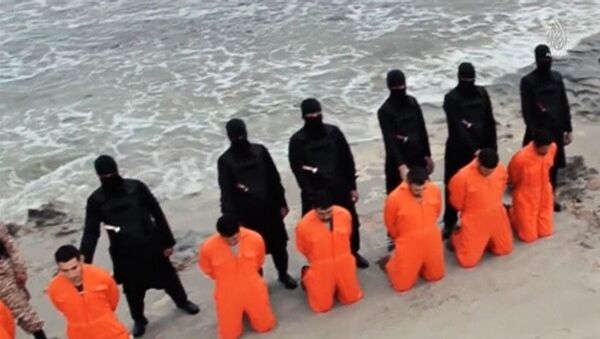 Men in orange jumpsuits purported to be Egyptian Christians held captive by the Islamic State (IS) kneel in front of armed men along a beach said to be near Tripoli, in this still image from an undated video made available on social media on February 15, 2015. - Sputnik Afrique
