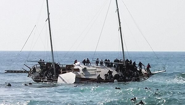 Migrants, who are trying to reach Greece, are seen onboard a capsized sailboat, as others are seen in the water trying to reach the coast of the southeastern island of Rhodes April 20, 2015 - Sputnik Afrique