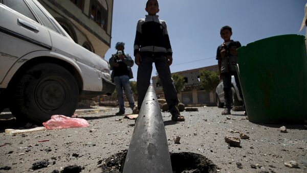 Boys stand in front of an artillery shell partially buried in the ground along a street damaged by an air strike on Monday that hit a nearby army weapons depot, in Sanaa April 21, 2015. - Sputnik Afrique