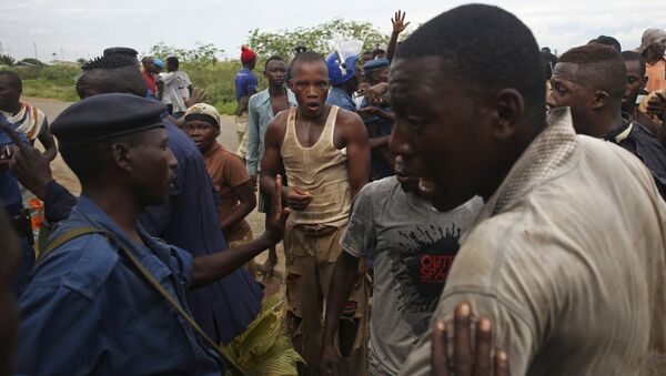 Protesters gesture near female police officer accused of shooting a protestor in Buterere neighbourhood of Bujumbura, Burundi - Sputnik Afrique