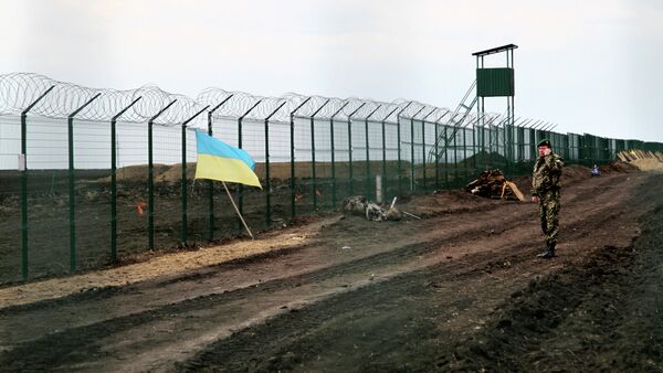 A Ukrainian border guard officer speaks on a phone near a national flag attached to the fence on the Ukrainian-Russian border near Hoptivka, Kharkiv region, eastern Ukraine - Sputnik Afrique