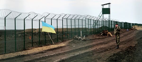 A Ukrainian border guard officer speaks on a phone near a national flag attached to the fence on the Ukrainian-Russian border near Hoptivka, Kharkiv region, eastern Ukraine - Sputnik Afrique