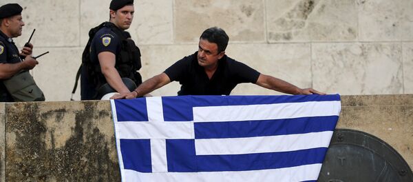An anti-EU protester unfurls a Greek national flag next to riot police on the steps in front of the parliament building during a demonstration of about five hundred people in Athens, Greece July 13, 2015. - Sputnik Afrique