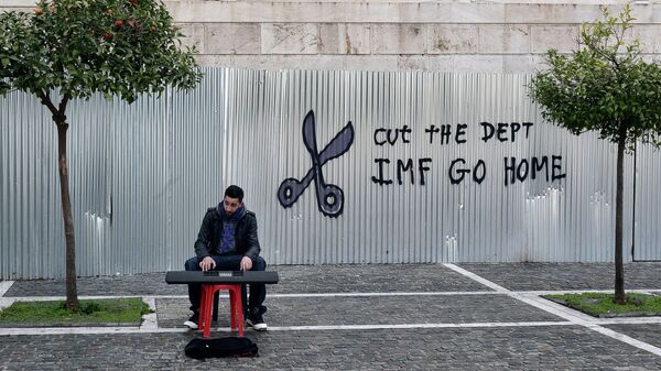 A man plays music on a digital keyboard near graffiti on a corrugated metal gate reading Cut the debt, IMF go home in Athens on February 24, 2015 - Sputnik Afrique