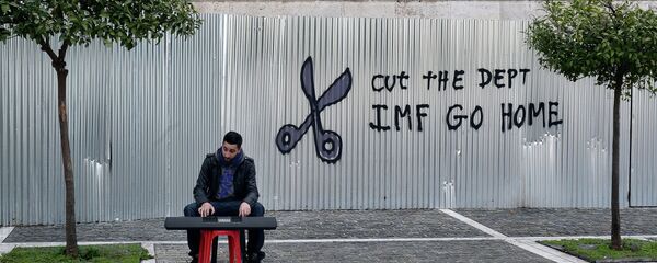 A man plays music on a digital keyboard near graffiti on a corrugated metal gate reading Cut the debt, IMF go home in Athens on February 24, 2015 - Sputnik Afrique