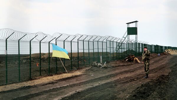 A Ukrainian border guard officer speaks on a phone near a national flag attached to the fence on the Ukrainian-Russian border near Hoptivka, Kharkiv region, eastern Ukraine - Sputnik Afrique