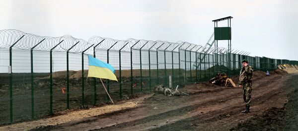 A Ukrainian border guard officer speaks on a phone near a national flag attached to the fence on the Ukrainian-Russian border near Hoptivka, Kharkiv region, eastern Ukraine - Sputnik Afrique