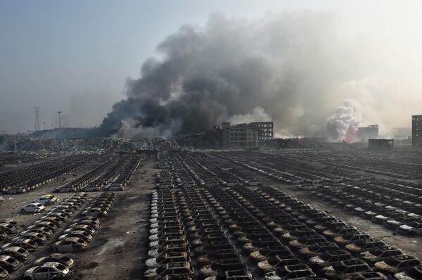 Smoke billows behind rows of burnt out cars at the site of a series of explosions in Tianjin, northern China on August 13, 2015. - Sputnik Afrique