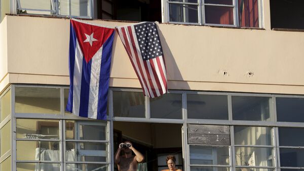 Cuban residents living next to the U.S. embassy look out of a window underneath the Cuban and U.S. flags in Havana, Cuba, August 14, 2015 - Sputnik Afrique