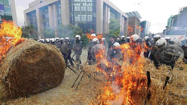 Belgian riot police officers stand guard while demonstrators burn hay as farmers and dairy farmers from all over Europe take part in a demonstration outside an European Union farm ministers emergency meeting at the EU Council headquarters in Brussels, Belgium, September 7, 2015. - Sputnik Afrique
