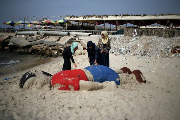 Palestinian girls put flowers on a sand sculpture depicting Syrian boy Aylan Kurdi, a three-year-old boy who drowned off Turkey, on September 7, 2015, on Gaza city beach - Sputnik Afrique
