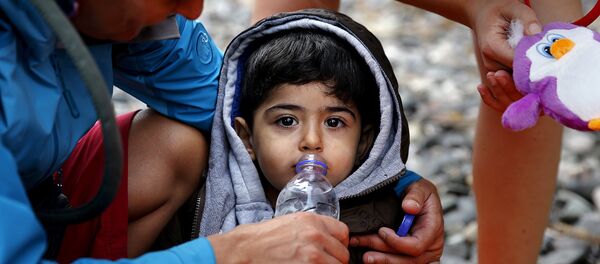 Une volontaire donne à boire à un petit réfugié syrien - Sputnik Afrique