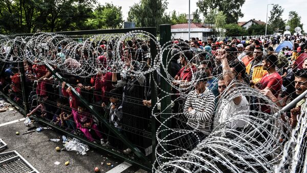 Refugees stand behind a fence at the Hungarian border with Serbia near the town of Horgos on September 16, 2015 - Sputnik Afrique