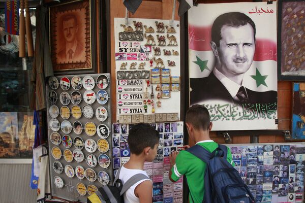 Des écoliers choisissent un souvenir dans un magasin où il y a le portrait de Bachar el-Assad avec la phrase On vous aime marqué dessus, Damas, Syrie - Sputnik Afrique