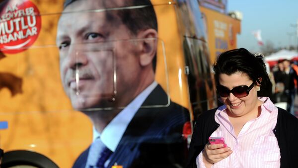A Turkish woman looks at her smartphone as she walks by a banner displaying a portrait of Turkish prime minister Recep Tayyip Erdogan, in Istanbul, on March 21, 2014 - Sputnik Afrique