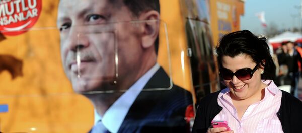 A Turkish woman looks at her smartphone as she walks by a banner displaying a portrait of Turkish prime minister Recep Tayyip Erdogan, in Istanbul, on March 21, 2014 - Sputnik Afrique