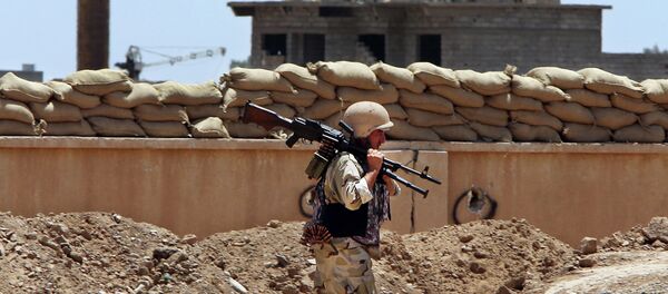 A Kurdish Peshmerga fighter carries his weapon walks onto his base, where two flags of the Islamic State in Iraq and the Levant (ISIL) are seen on a building, right, and water tower, left, at the front line with the al-Qaida-inspired militants in Tuz Khormato, 100 kilometers (62 miles) south of the oil rich province of Kirkuk, northern Iraq. - Sputnik Afrique