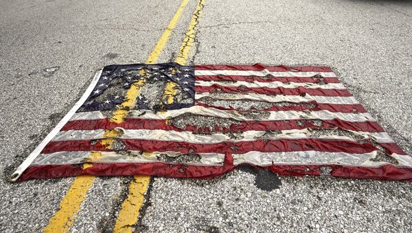 A partially burned American flag lies on the street near the spot where Michael Brown was killed before an event to mark the one year anniversary of his killing in Ferguson, Missouri August 9, 2015 - Sputnik Afrique
