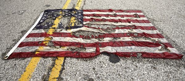 A partially burned American flag lies on the street near the spot where Michael Brown was killed before an event to mark the one year anniversary of his killing in Ferguson, Missouri August 9, 2015 A partially burned American flag lies on the street near the spot where Michael Brown was killed before an event to mark the one year anniversary of his killing in Ferguson, Missouri August 9, 2015 - Sputnik Afrique