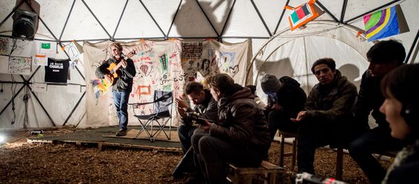 migrants écoutent un guitariste dans un théâtre improvisée, Calais - Sputnik Afrique