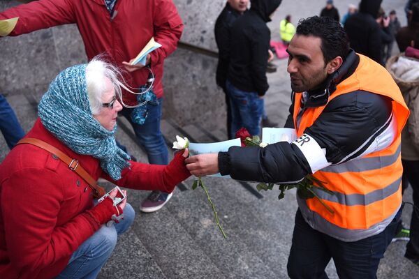 Des réfugiés syriens offrent des fleurs aux passants lors d'une manifestation contre les violences organisée le 16 janvier près de la gare de Cologne, en Allemagne de l'ouest, où des centaines de femmes ont été violées par des migrants. Des réfugiés syriens offrent des fleurs aux passants lors d'une manifestation contre les violences organisée le 16 janvier près de la gare de Cologne, en Allemagne de l'ouest, où des centaines de femmes ont été violées par des migrants. - Sputnik Afrique