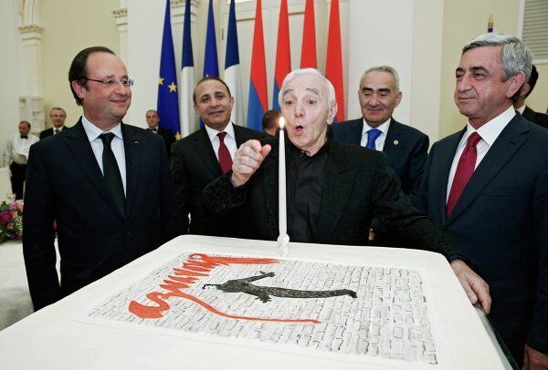 Charles Aznavour soufflant une bougie sur le gâteau offert à l'occasion de ses 90 ans lors du dîner officiel organisé à Erevan par le président arménien Serge Sargsian (à droite) en l'honneur du président français François Hollande (à gauche). - Sputnik Afrique