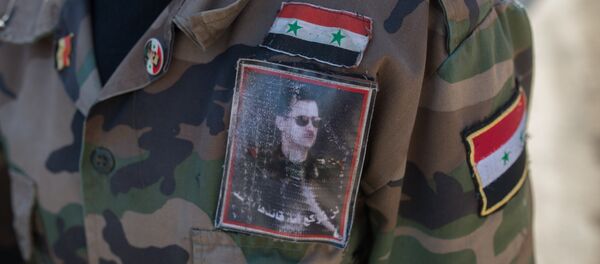 Un volontaie de l'armée syrienne porte un uniforme à l'effigie du président Assad - Sputnik Afrique