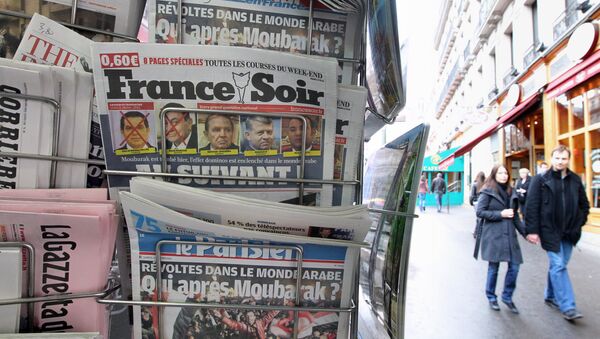 People are seen walking behind French daily newspapers displayed at a news kiosk in Paris. (File) - Sputnik Afrique