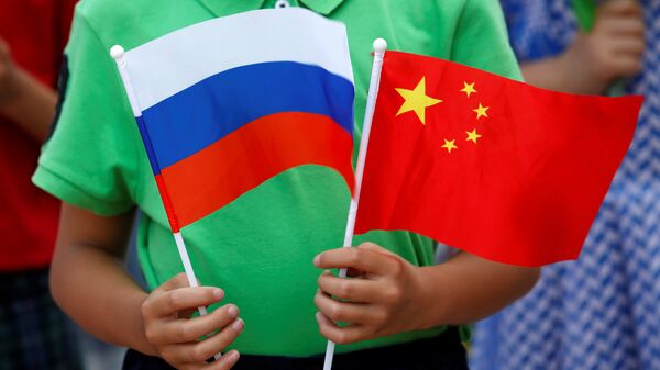Un enfant tient des drapeaux russe et chinois lors de la cérémonie d'accueil du président russe Vladimir Poutine à Pékin - Sputnik Afrique