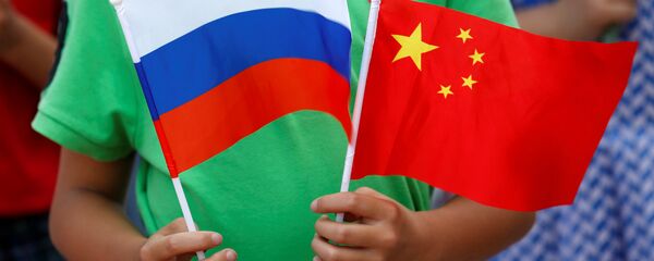 Un enfant tient des drapeaux russe et chinois lors de la cérémonie d'accueil du président russe Vladimir Poutine à Pékin - Sputnik Afrique