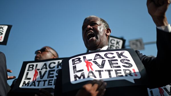 Une homme porte une pancarte Black Lives Matter lors d'une marche en l'honneur de Martin Luther King Jr. - Sputnik Afrique