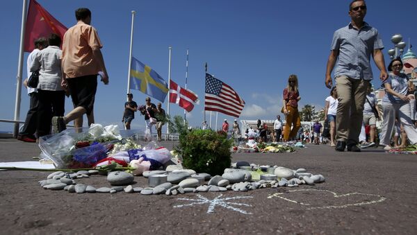 People walk past a heart shape makeshift memorial with a U.S. flag placed on the road in tribute to victims before a minute of silence on the third day of national mourning in France. Nice, July 18, 2016 - Sputnik Afrique