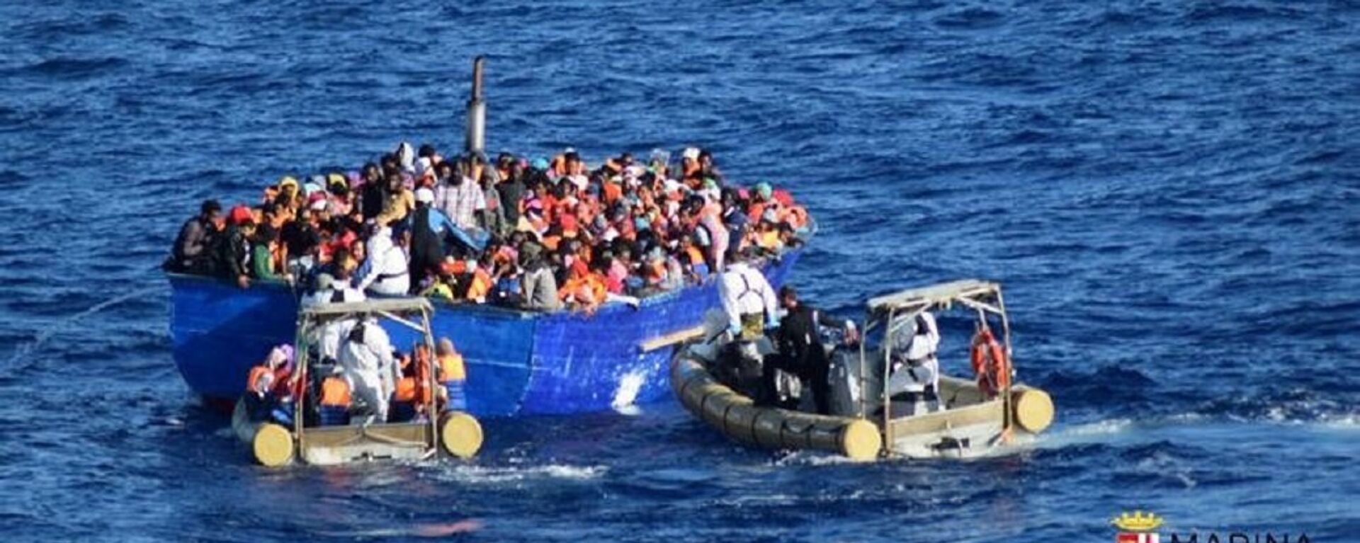 Migrants sit in their boat during a rescue operation by Italian navy ship Borsini (unseen) off the coast of Sicily, Italy, in this handout picture courtesy of the Italian Marina Militare released on July 19, 2016. - Sputnik Afrique, 1920, 18.06.2021