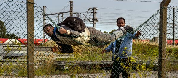 A migrant climbs over a fence in Coquelles, near Calais northern France - Sputnik Afrique