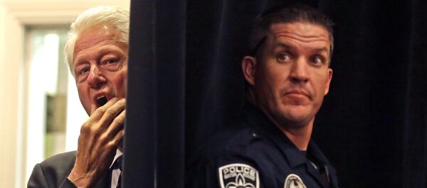 A Baton Rouge police officer stands post while former President Bill Clinton, left, watches from backstage before he is introduced to speak at a campaign event for Sen. Mary Landrieu, D-La., in Baton Rouge, La., Monday, Oct. 20, 2014. - Sputnik Afrique