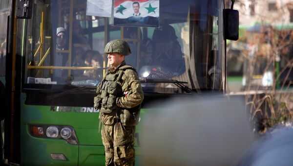 Un soldat russe à côté d'un bus qui a ramené des civils à Alep - Sputnik Afrique