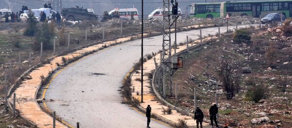 Members of the Syrian government forces stand guard near buses and ambulances during an evacuation operation of Syrian rebel fighters and civilians from a opposition-held area of Aleppo towards rebel-held territory in the west of Aleppo's province on December 16, 2016 - Sputnik Afrique