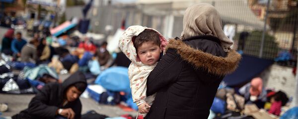 A Syrian woman holds her child at the port of Chios on April 3, 2016 as refugees and migrants who broke out from Chios detention camp, stand in the port of the city. - Sputnik Afrique