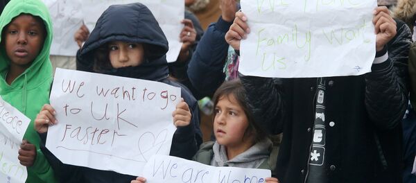 Young migrants pose with posters reading 'We want to go faster to UK' and 'We have family waiting for us' at the Jungle migrant camp in Calais, northern France, on October 26, 2016, during a massive operation to clear the squalid settlement where 6,000-8,000 people have been living in dire conditions. Workers ramped up demolition of France's notorious Calais Jungle on October 26, 2016 - Sputnik Afrique