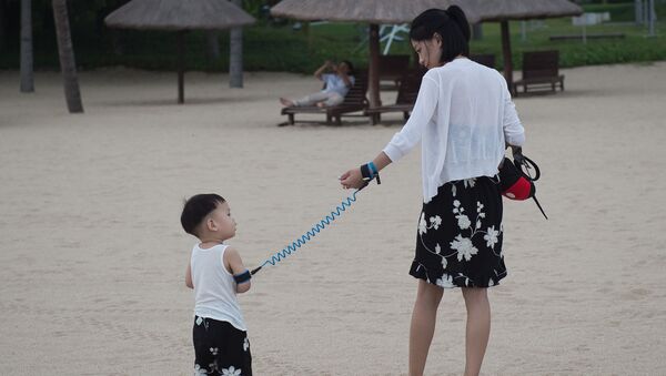 In this picture taken on October 11, 2016 a mother is using a leash to keep her child nearby at a beach at the Club Med resort in Sanya. - Sputnik Afrique
