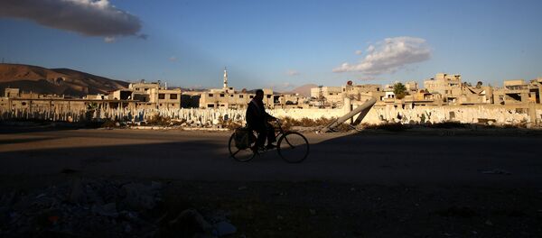A man rides a bicycle near a cemetery in the rebel held besieged town of Douma, eastern Ghouta in Damascus, Syria - Sputnik Afrique