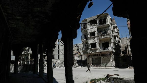 Syrians walk past damaged buildings on April 7, 2017, in the rebel-held town of Douma, on the eastern outskirts of Damascus. - Sputnik Afrique