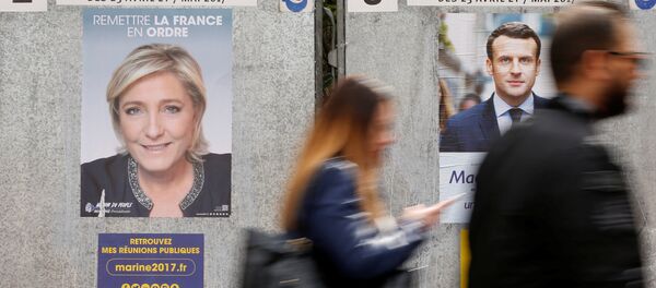 People walk past campaign posters of Marine Le Pen (L), French National Front (FN) political party leader, and Emmanuel Macron (R), head of the political movement En Marche! (Onwards!), two of the eleven candidates who run in the 2017 French presidential election in Paris, France, April 10, 2017 - Sputnik Afrique