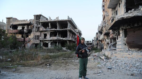 In this Feb. 23, 2016 file photo, a civilian fighter holding the Libyan flag stands in front of damaged buildings in Benghazi, Libya - Sputnik Afrique