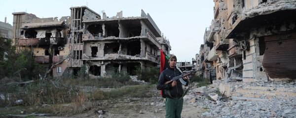 Un combattant civil tient un drapeau libyen preès des bâtiments endommagés à Benghazi, en Libye - Sputnik Afrique