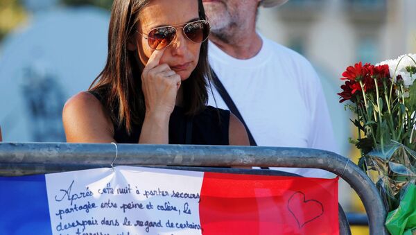 A woman reacts near flowers and flags placed in tribute to victims, two days after an attack by the driver of a heavy truck who ran into a crowd on Bastille Day killing scores and injuring as many on the Promenade des Anglais, in Nice, France, July 16, 2016. - Sputnik Afrique