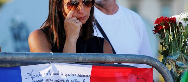 A woman reacts near flowers and flags placed in tribute to victims, two days after an attack by the driver of a heavy truck who ran into a crowd on Bastille Day killing scores and injuring as many on the Promenade des Anglais, in Nice, France, July 16, 2016. - Sputnik Afrique