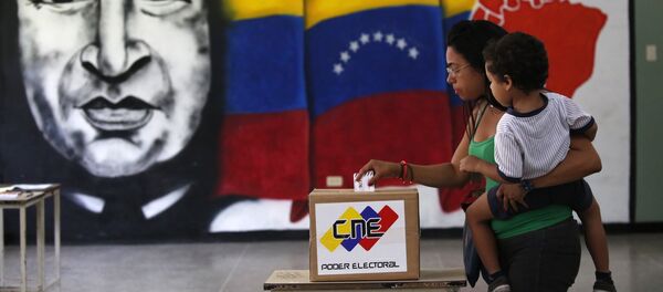 A woman holds her infant as she casts her vote in front of a mural of the late Venezuelan President Hugo Chavez at a polling station during the Constituent Assembly election in Caracas, Venezuela, July 30, 2017. - Sputnik Afrique
